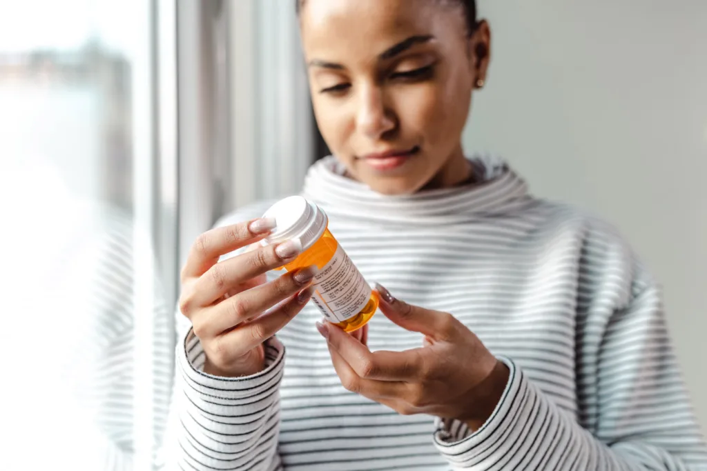 A young woman standing by the window and holding medicine bottle